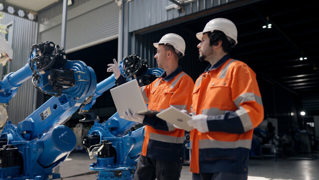 Robotics technician team using laptop inspect refurbished industrial robot arm systems at warehouse. plant engineering, automatic factory, installation, robotics system integration.