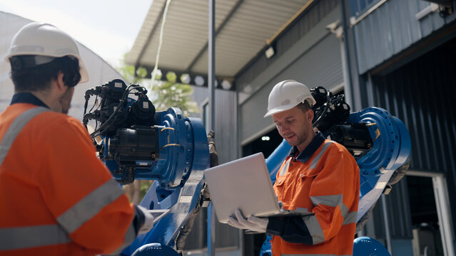 Robotics specialists team discussing refurbished industrial robot arm systems at warehouse. plant engineering, smart manufacturing, automatic factory, installation, robotics system integration.