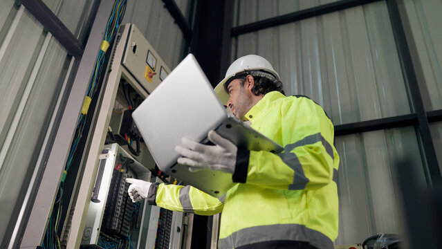 Electrical technician working inspecting electrical control panel in industrial factory, supporting preventive maintenance, diagnostic, troubleshooting, safety, efficiency, compliance.