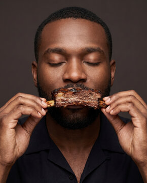 Primal man bites into smoky barbecue ribs, with closed eyes with rich color and texture