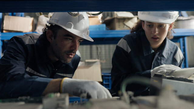 Maintenance technicians check spare part for on warehouse shelves, using tablet for parts identification, inventory control, maintenance planning, repair, reliability.