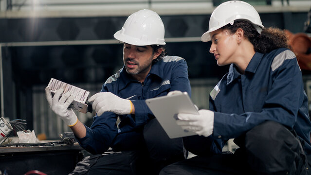 Engineer examines electronic scrap and machine parts in factory, using tablet for waste management, responsible disposal, factory sustainability campaign, conservation.