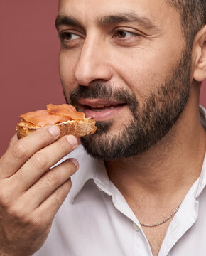 Weathered man eats a slice of bread with smoked salmon, with a smile with rich color and texture