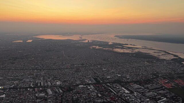City sprawls below as sun dips low. Orange hues bleed into fading twilight at Surabaya