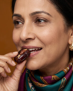 Sensory woman bites a stuffed date, with elegance against a solid studio background