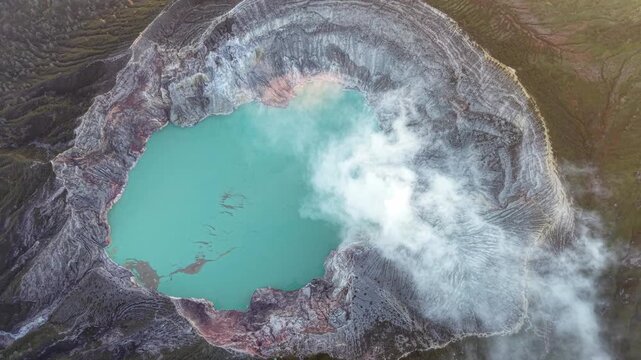 Top down drone shot of Mount Ijen turquoise crater lake with steaming fumaroles and rocky caldera
