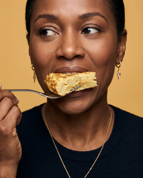 Hearty woman eats a forkful of Spanish tortilla, with satisfaction with striking studio color