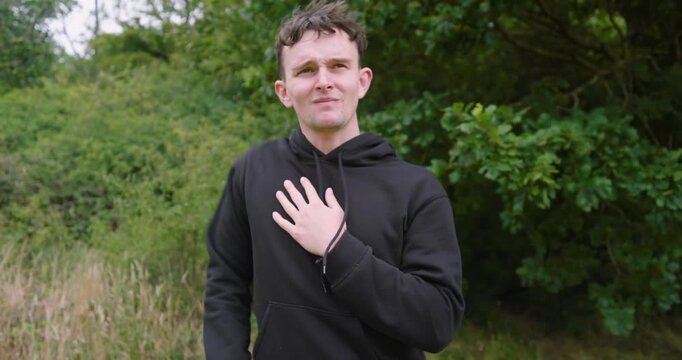 Man in black hoodie stretching arm outdoors, preparing for run in nature