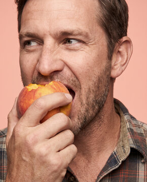Fresh man bites into a ripe peach, outdoors with rich color and texture
