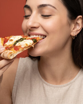 Indulgent woman bites a cheesy pizza slice, with a smile in an intimate close crop