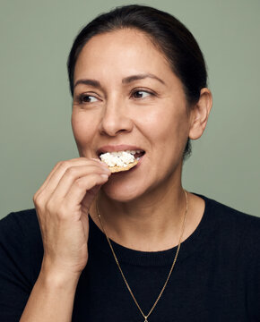 Sensory woman eats a piece of bread and cheese, with a smile against a saturated backdrop