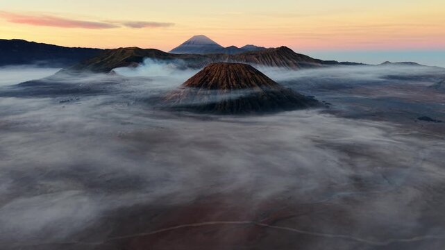 Misty dawn wraps volcanic peaks in soft, drifting clouds. Sunlight blushes the horizon