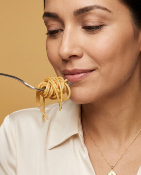 Composed woman eats a forkful of spaghetti, with a gentle smile in an intimate close crop
