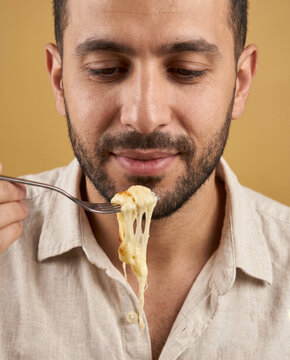 Hearty man eats a forkful of cheesy pasta, with satisfaction against a saturated backdrop