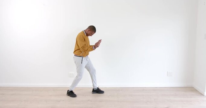 African American man dancing energetically in casual outfit against white wall