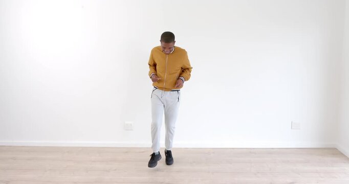 Young man dancing joyfully in casual outfit against white wall indoors
