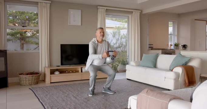 Older senior man exercising with dumbbells in living room, staying active at home