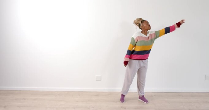 Woman in colorful sweater dancing energetically in bright, minimalist room