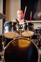 Obraz premium Bald male drummer playing drum kit during studio rehearsal under warm light