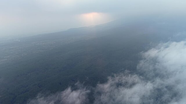 Misty aerial panorama of Wonosari tea plantation with clouds, rolling hills and soft sunrise light.