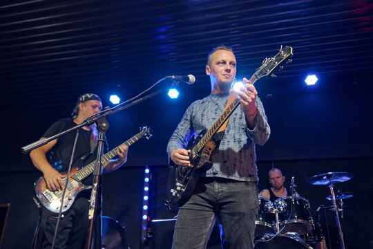 Adult male guitarist performs during band sound check under blue stage lights