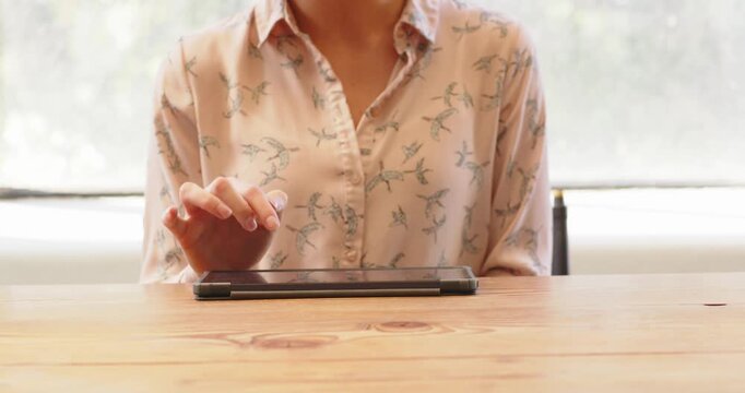 Woman in patterned blouse using tablet on wooden desk in bright office