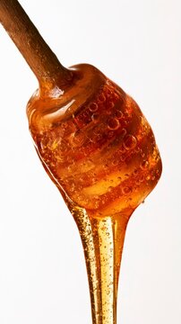 Viscous golden honey dripping from a wooden dipper on a white background