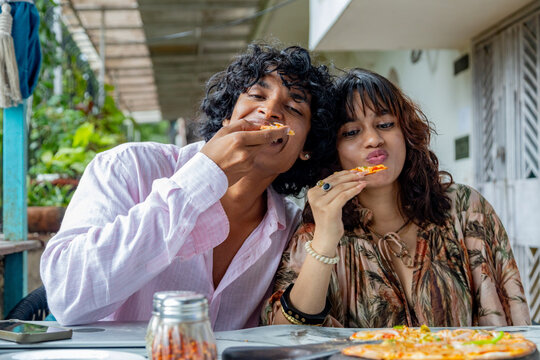 Young Indian Gen Z man and woman enjoying pizza together at a modern caf&eacute;, sharing a casual meal and social moment, friendship, youth lifestyle, urban life in India.