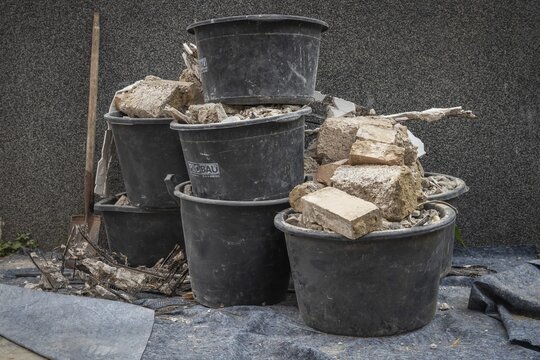 Construction waste in several black buckets stands in a courtyard in front of a wall against which a shovel is leaning, Stuttgart, Baden-W&uuml;rttemberg, Germany