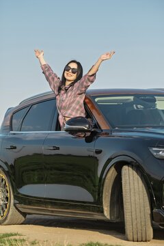 A woman with long black hair celebrates a sunny day by extending her arms out of a car window