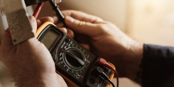 Close-up of hands using a multimeter for electrical testing.