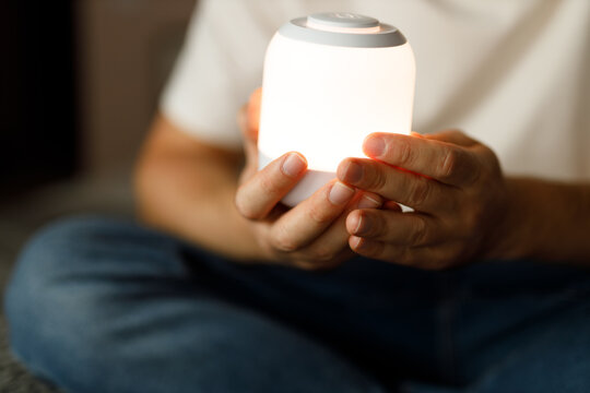Person holding glowing bedside night light for relaxation background and cozy home interior scene for wellness design