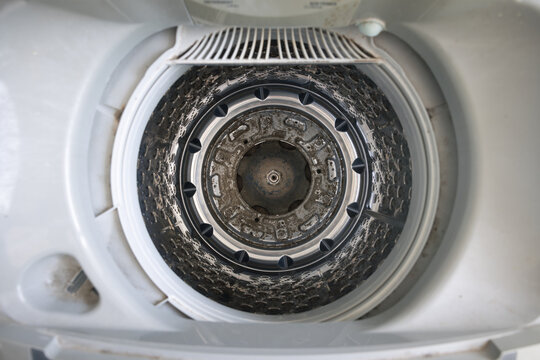 Dirty washing machine tub interior with mold, detergent residue, mineral buildup and grime around drum base, showing appliance hygiene problem, household maintenance, cleaning service concept.