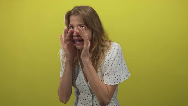 Woman cupping hands near mouth in studio by lime green wall, wearing white polka dot dress and holding open palms in an emphatic pleading gesture; panic.