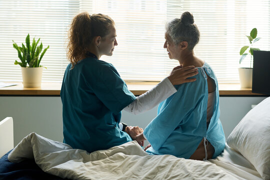 Caucasian young adult nurse supporting senior woman patient in hospital bed, showing empathy. Concept represents healthcare and geriatric medicine for medical marketing campaigns