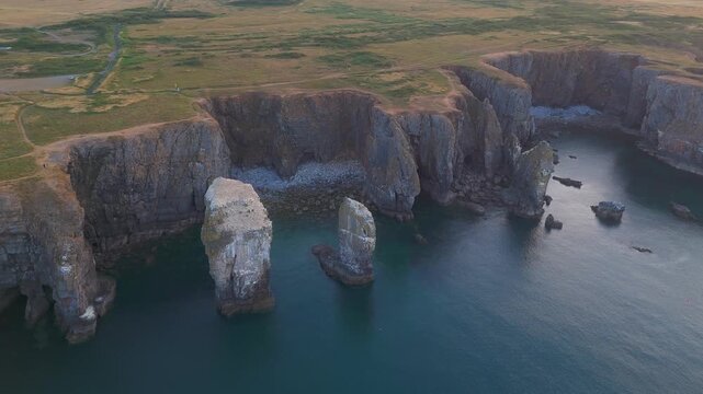 Aerial orbit around the limestone sea stacks and rugged coastal cliffs at Elegug Stacks on the Pembrokeshire Coast, Wales.