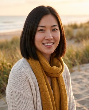 Contemplative Asian woman smiling in mustard scarf on windy autumn beach dunes path