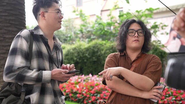 Two men look down at a smartphone while another person holding a camera stands close by outdoors.