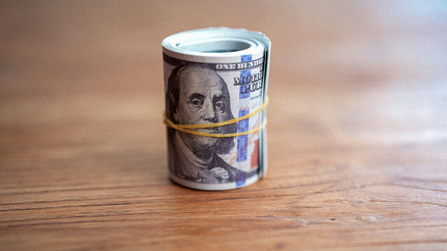 Close-up of rolled US dollar banknotes secured with rubber bands on a wooden table. Concept of money, savings, cash, finance, investment and personal wealth.