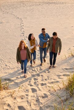 Diverse friends walking down sandy dune path leaving footprints behind them