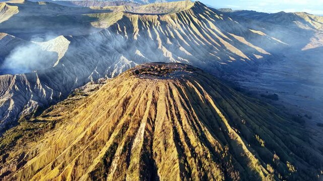 Golden light bathes volcanic Mount Batok peaks. Smoke drifts from crater rim