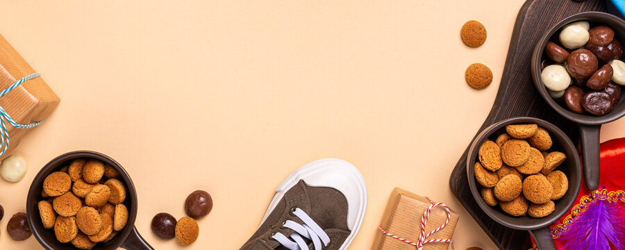 Overhead view banner shows cookies, chocolates, wrapped presents, a sneaker and colorful holiday decoration arranged around open peach space. Dutch Belgium holiday Sinterklaas with copy space