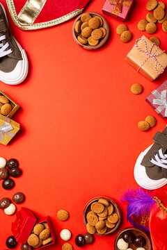 Sinterklaas holiday Sint Nicholas day arrangement shows Dutch spiced cookies pepernoten, wrapped gifts, shoes and a festive hat around a bright red background, top view with copy space