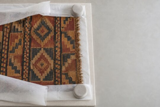 Original geometric woven textile laid flat on archival supports beside neutral conservation weights and acid-free tissue during preservation readiness in modern Andean regional museum conser
