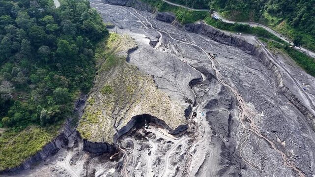 Excavator machinery digging through thick volcanic sand deposits inside a deep river channel at the foot of Mount Semeru.