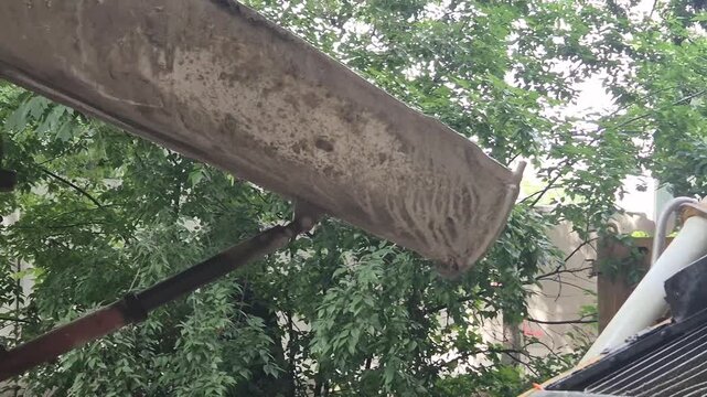 Side view of a concrete mixer truck reversing towards the hopper of a concrete pump on a construction site.