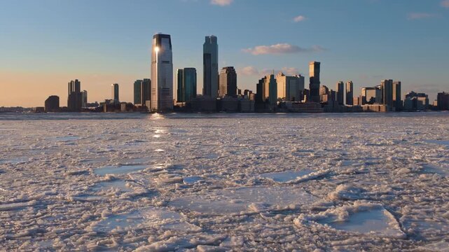 Drifting ice floes in frozen Hudson River at sunset with Downtown Jersey City skyline during extreme winter cold