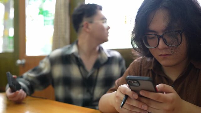 A man in a brown shirt looks down at a smartphone while seated at a restaurant table.