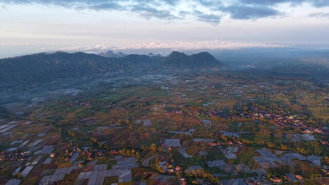 Expansive terraced rice paddies at dawn with mountain ridge and scattered village under pastel sky.