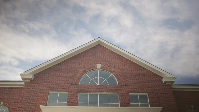 Low angle view of a red brick building facade with a gabled roof against a cloudy blue sky